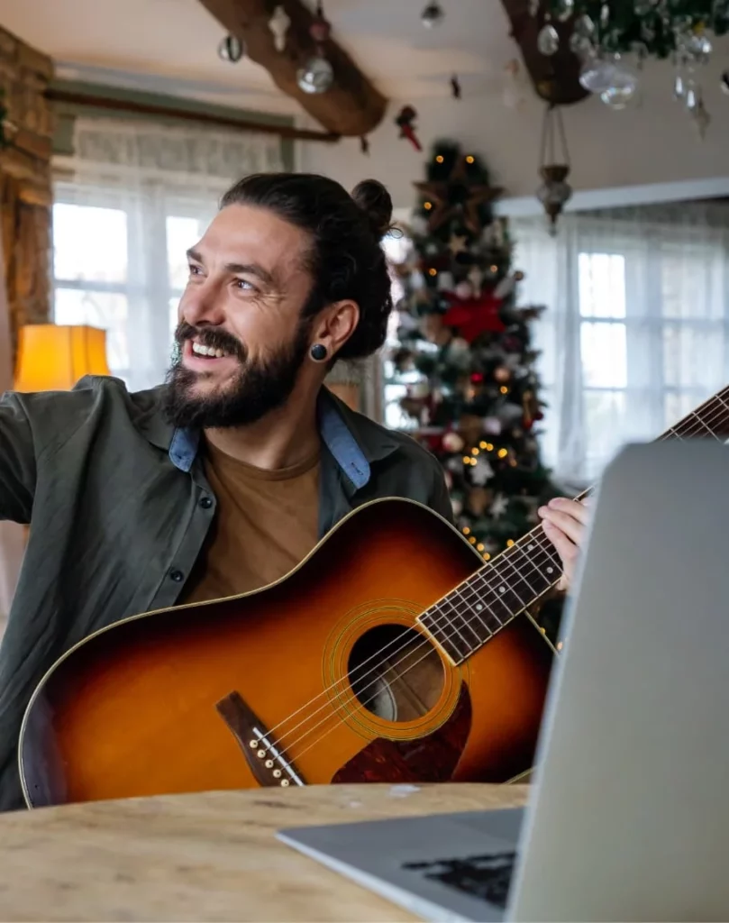 Uśmiechnięty mężczyzna grający na gitarze przed choinką - radosna nauka języka obcego online i wspólne śpiewanie kolęd po angielsku.