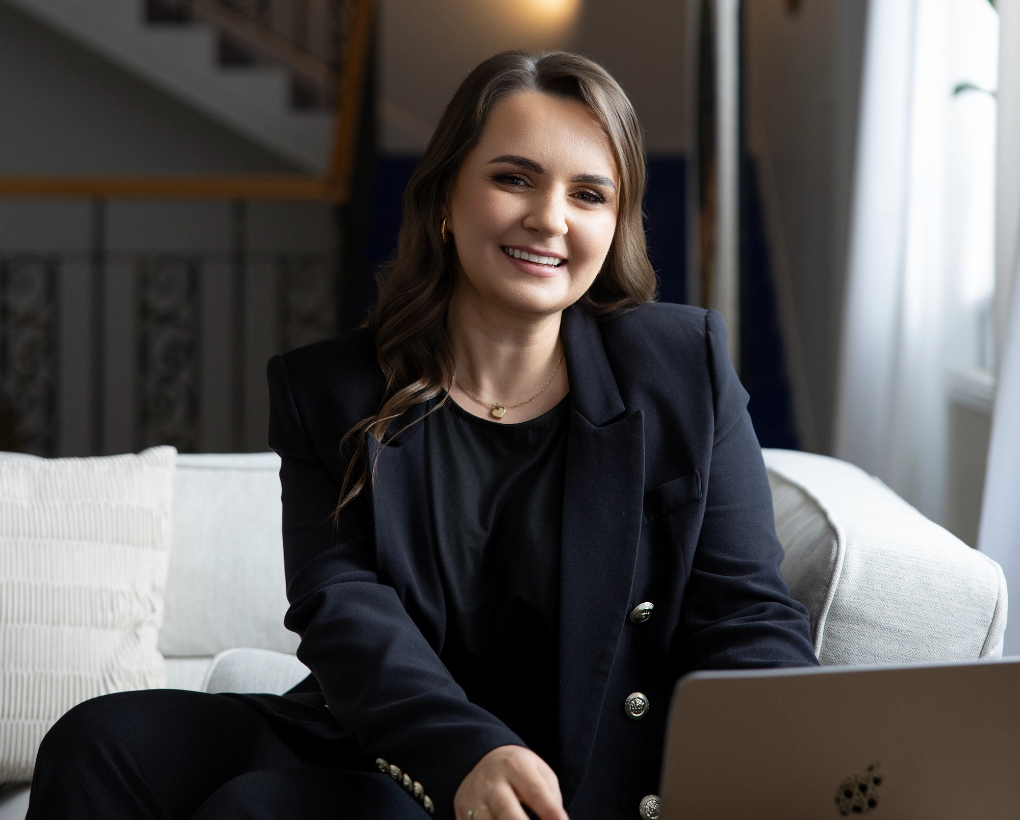Uśmiechnięta założycielka szkoły językowej SpeakPro Academy w eleganckiej marynarce przy laptopie, reprezentująca zespół doświadczonych lektorów języków obcych.
